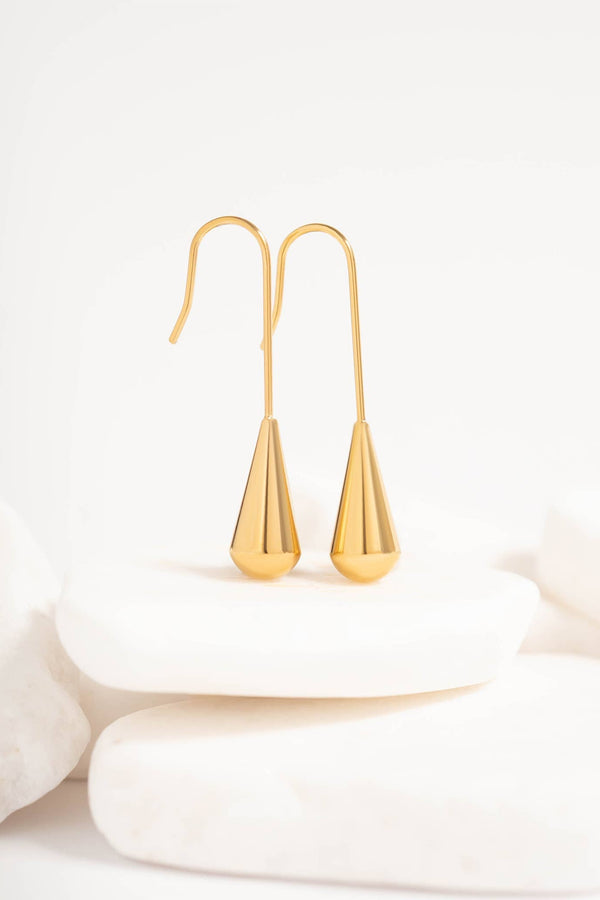 Gold teardrop earrings on a white surface with a light background
