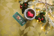 Load image into Gallery viewer, Candle and packaging on a decorative surface with Christmas decorations