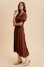 Load image into Gallery viewer, Woman wearing a brown dress with puffed sleeves and tiered skirt on a beige background