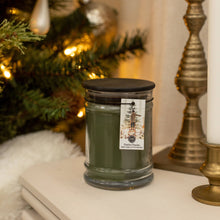 Load image into Gallery viewer, Green candle with a label in front of a decorated Christmas tree