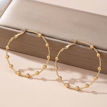 Load image into Gallery viewer, Gold hoop earrings with bead detailing on a beige surface