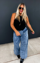 Load image into Gallery viewer, Woman wearing a black top and blue jeans against a dark wall.