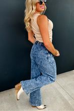 Load image into Gallery viewer, Woman wearing a beige top and blue jeans against a black wall.
