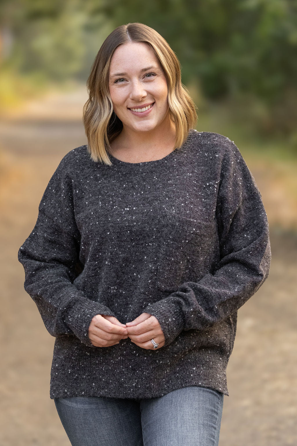 Woman wearing a dark gray speckled sweater outdoors with a blurred natural background