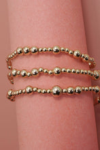 Load image into Gallery viewer, Gold beaded bracelet on a wrist against a pink background