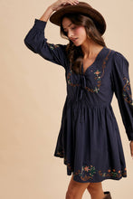 Load image into Gallery viewer, Woman wearing a navy dress with floral embroidery and a brown hat against a beige background