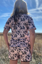 Load image into Gallery viewer, Person wearing a patterned outfit with horses in an open field