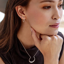 Load image into Gallery viewer, Close-up of a woman wearing silver earrings and a necklace, with one hand on her chin.