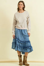 Load image into Gallery viewer, Woman wearing a beige sweater and blue ruffled skirt with cowboy boots on a beige background