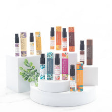 Load image into Gallery viewer, Collection of small spray bottles with colorful labels on a white stand.