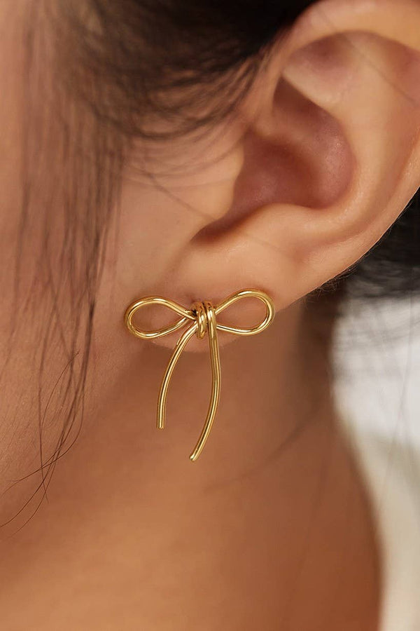 Gold bow-shaped earring worn on an ear