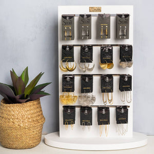 Display of Scout earrings on a white stand with a plant beside it.