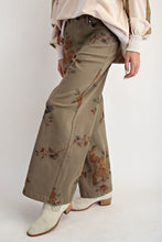 Load image into Gallery viewer, Woman wearing olive trouser with flower pant against white background wall