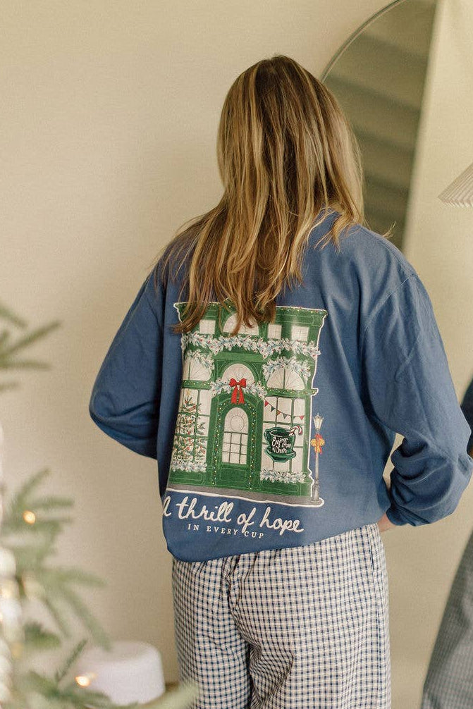Person wearing a blue sweatshirt with a design on the back, standing in front of a mirror next to a Christmas tree.