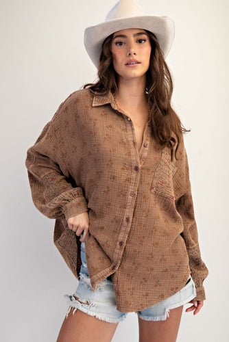 Woman wearing a brown textured shirt and denim shorts with a white hat on a plain background