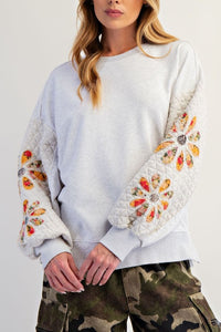 woman wearing grey colored sweatshirt with quilted sleeves with flower patches