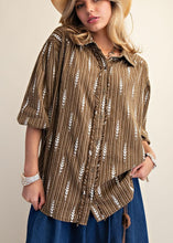 Load image into Gallery viewer, A woman wearing a brown and beige vertically striped button-up shirt with white leaf patterns, a beige cowboy hat, and a blue skirt, posing against a neutral beige background.