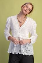 Load image into Gallery viewer, Woman wearing a white blouse with long sleeves and black pants against a green background