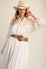 Load image into Gallery viewer, A woman wearing a cream-colored bohemian-style maxi dress with embroidered details, a wide brown woven belt, and a straw cowboy hat, posed against a solid beige background.
