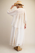 Load image into Gallery viewer, A woman shown from the back wearing a cream-colored bohemian-style maxi dress with a textured crinkle fabric, long sleeves, and a lace-trimmed hem, paired with a straw hat and tan boots against a solid beige background.