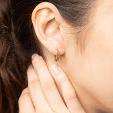 Load image into Gallery viewer, Close-up of a person wearing gold hoop earrings with a blurred background