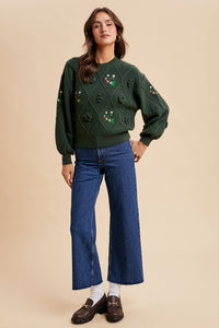 Woman wearing a green patterned sweater and blue jeans on a beige background