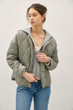 Load image into Gallery viewer, Woman wearing a green quilted jacket with a gray hood against a white background