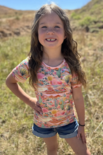 Load image into Gallery viewer, Young girl wearing a colorful desert-themed shirt in a natural setting