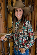 Load image into Gallery viewer, Woman wearing a patterned shirt and cowboy hat in a rustic setting with wooden walls and horse equipment.